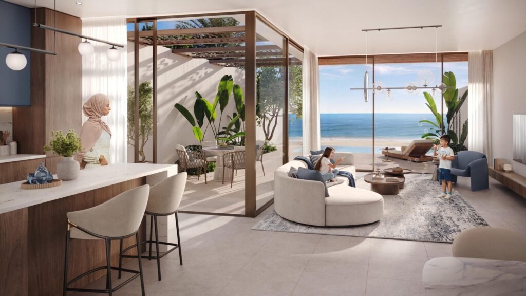 Modern living room with a view of the ocean, featuring a light-colored circular sofa, a coffee table, and a dining area with outdoor seating. A woman in a hijab, a boy, and a girl are present, adding a homey atmosphere. Lush greenery is visible through large windows.