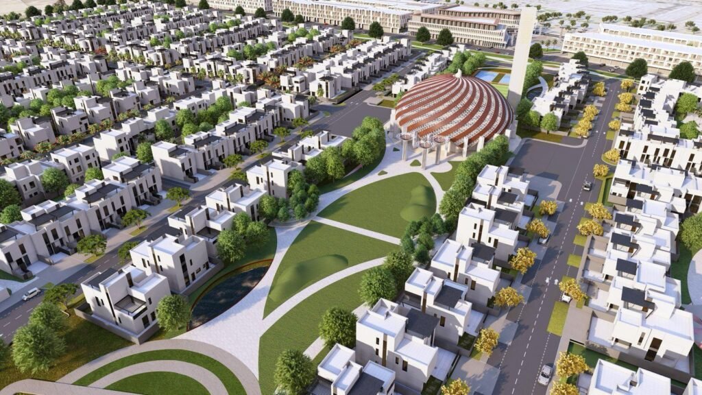An aerial view of a modern residential area featuring numerous white houses surrounded by trees and green spaces, with a distinct circular building and pathways visible in the center.